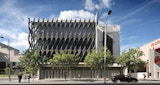 Commercial Architecture building with metal geometric cladding on upper three levels. Street view with parked black car, trees, adjacent buildings and pedestrians.