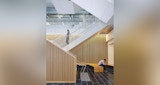 ABC headquarters south Brisbane Queensland Internal stairwell details. vertical timber battens line stair walls and far wall behind. Woman in profile walking down stairs. Man seated on timber bench seating in lobby.