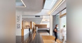 ABC Headquarters ground level entry/reception. Two women in blur exit through glass entry doors. ABC logo printed vertically on the left wall with timber accented reception desk behind running the length of the front lobby. Black tile floors.