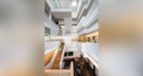 Internal multi-level lobby / stairwell of ABC headquarters in South Brisbane Queensland, designed by KIRK Studio. Four level timber staircases with people walking about on each level. Bright white walls and balustrade.