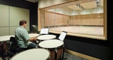Media production studio inside the KIRK studio designed ABC Headquarters building in Southbank, Australia. Man playing drum inside black sound and media production room.  internal timber framed window view from media studio into symphony rehearsal space.