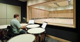 Media production studio inside the KIRK studio designed ABC Headquarters building in Southbank, Australia. Man playing drum inside black sound and media production room. internal timber framed window view from media studio into symphony rehearsal space.