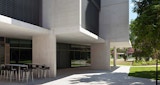 Ground level patio external seating with black chairs under building with paved pedestrian space near green landscaped tree outside the KIRK studio designed ABC Headquarters building in Southbank, Australia.