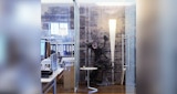 Glass office space with desk and files connected to hall. Timber floor with view to vintage iron printing press against brick wall.