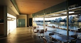 internal room with lights off but illuminated by bright afternoon sun. Room has a full floor to ceiling wall of glass windows with small groups of tables and chairs placed inside as well as outside on balcony. View of the adjacent Brisbane River and city beyond.