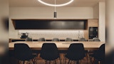 Staff kitchen inside modern office. Double sided seating timber island with 12 black chairs. White tile splash back.