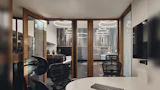 Meeting room inside modern office space. timber framed glass door and partition wall looking into rest of office space. TV hanging on wall.