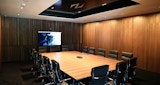 large conference room with large wood table and 15 black chairs. Tv hung on far wall with timber lined walls inside  inside the NIOA office Canberra, designed by KIRK studio Architects.