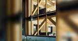 Close up view of ground and first floor from exterior of commercial mass engineered timber building, by KIRK Studio. View into open concept workplace at dusk.