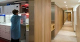 Blurred woman at work in dentistry lab with medical storage facilities and view down hall through clinic. Hall features timber batten feature walls inside Periocare Office architecture design Kirk Studio. 