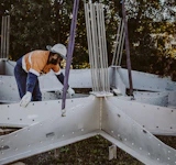 Construction worker assists the installation of timber beam connectors being erected onsite at mon repos turtle centre.
